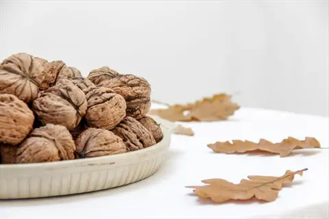 a bowl filled with walnuts on a white table, surrounded by autumn leaves