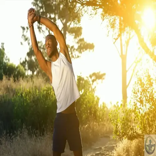 a man stretching flexibility by raising arms outdoors on a sunny trail with trees and grass