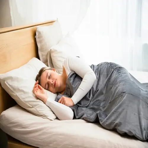 a woman sleeping peacefully on a bed with white pillows and gray blanket