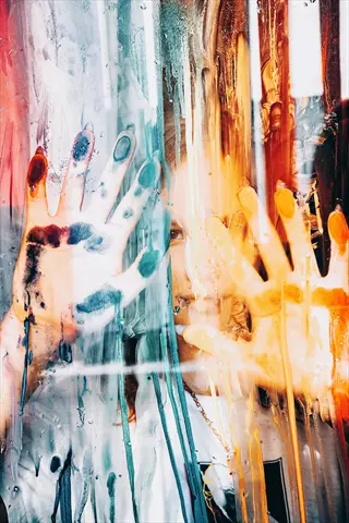 abstract art hands covered in paint press against a wet glass surface with vibrant drips; partially visible face obscured by colorful non-verbal expression
