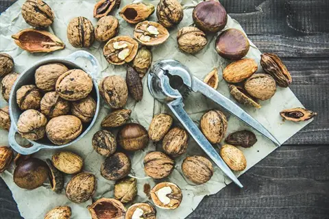 almonds, walnuts, and mixed nuts with nutcracker on parchment paper. rustic arrangement featuring whole, shelled, and cracked nuts in a bowl and scattered on a wooden surface