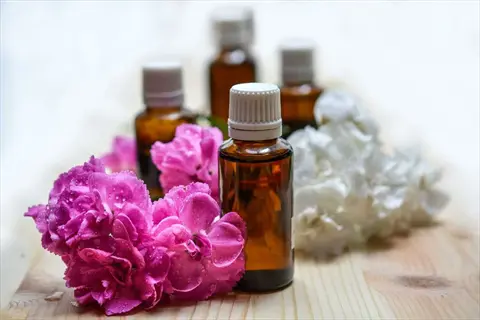 amber essential oil bottles with pink and white flowers on a wooden surface; these oils can be used as natural laundry fresheners