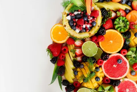 artistically arranged assorted fresh fruits including pineapple, berries, citrus slices, mango, kiwi, and more on a white background