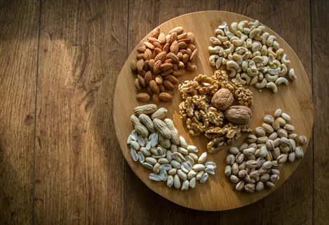 assortment of almonds, walnuts, seeds, and other nuts arranged in sections on a round wooden platter