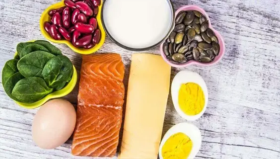 assortment of dietary minerals food including salmon, eggs, spinach, kidney beans, milk, pumpkin seeds and cheese arranged on a wooden surface
