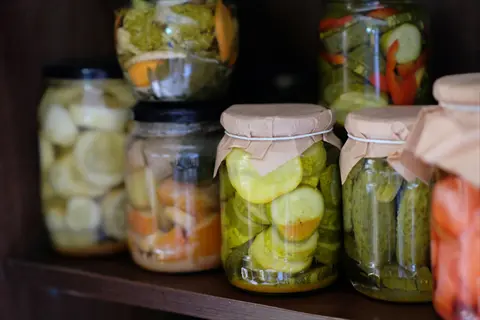 assortment of fermented vegetables jars featuring pickled cucumbers, sliced root vegetables, and mixed preserves displayed on rustic wooden shelves