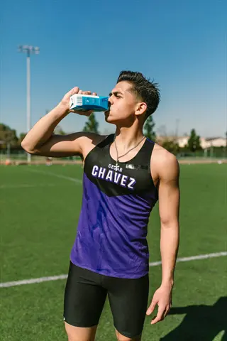 athlete drinking during game on a sunny sports field, wearing a purple-black 'cesar chavez' jersey while hydrating with a carton