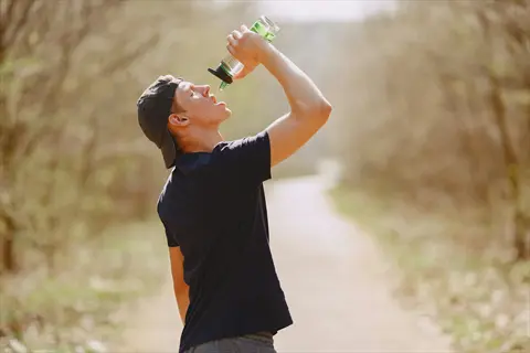 athlete drinking from water bottle during interval training on sunlit forest trail