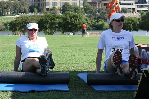 athletes using foam roller legs: two runners with race bibs (348) perform self-massage on foam rollers for leg recovery during outdoor relay event