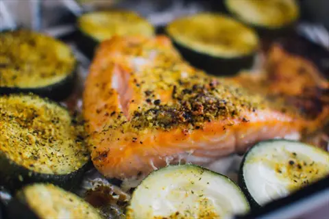 baking salmon with herbs alongside sliced zucchini vegetables in a baking dish