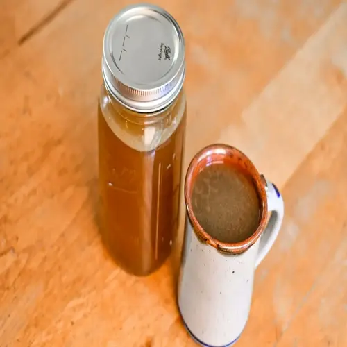 ball jar containing bone broth beside a ceramic coffee mug with brown rim on wooden surface; bone broth bowl concept