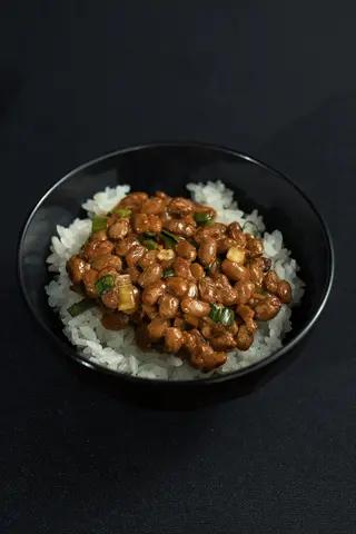 beans rice bowl: white rice topped with fermented natty beans and green onions in a black bowl. illustrates combination principles for complementary protein synergy