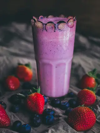blended berry smoothie in a tall glass with berry garnish, surrounded by fresh strawberries and blueberries