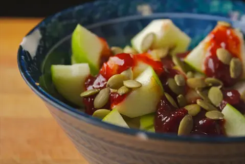 blue ceramic bowl of yogurt topped with green apple chunks, red berry compote, and roasted pumpkin seeds