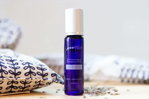 blue glass essential oil lavender bottle labeled 'lavender' with organic certification text, surrounded by textiles and dried lavender sprigs