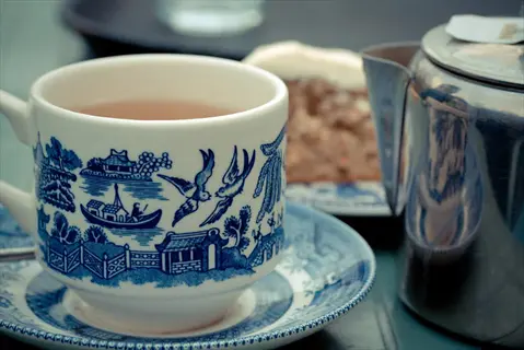 blue willow pattern peppermint tea cup and saucer with teapot and cake on table - digestive tea service