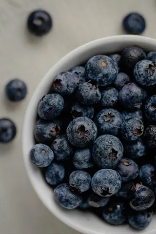 blueberries bowl: plump fresh blueberries overflowing from a white ceramic bowl on a linen surface