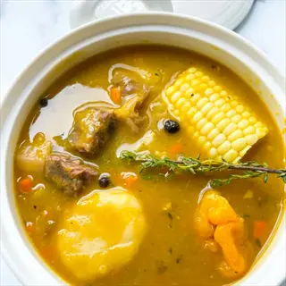 bone broth soup with corn, meat chunks, dumplings, carrots, and herbs in a white bowl