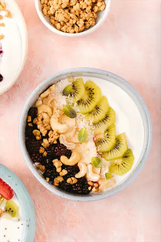 bowl of cashew berry parfait featuring creamy yogurt base, blackberries, cashews, kiwi slices, granola clusters, and fresh mint
