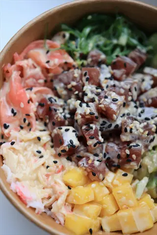bowl of colorful salad with black seeds, featuring tuna cubes, mango, avocado, seaweed, crab, and sesame seeds