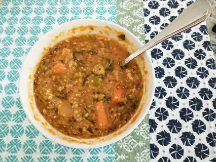 bowl of cooked lentils with carrots, vegetables, and spoon on patterned blue-green cloth - hearty plant-based meal
