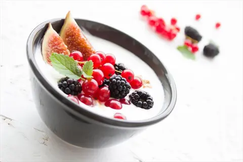 bowl of creamy yogurt topped with fresh berries (red currants, blackberries, figs) and mint, with scattered berries on a white surface