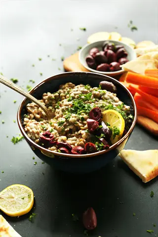 bowl of lentil dip with kalamata olives, lemon, parsley, served with carrot sticks and pita - lentil dip vegetables