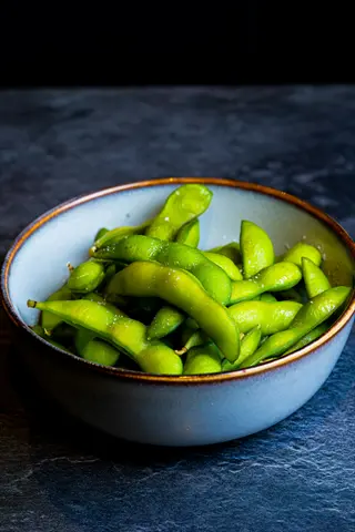 bowl of steamed edamame pods on dark surface - embodies 'edamame pods bowl' and 'edamame'