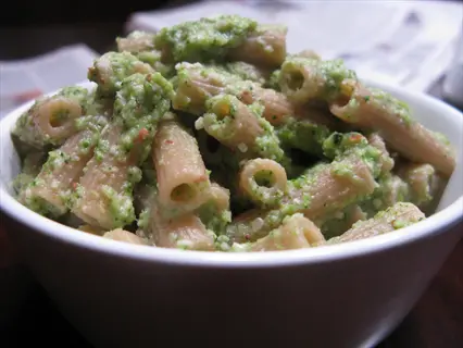 bowl of whole wheat pasta with green pesto sauce, light brown penne noodles on newspaper background