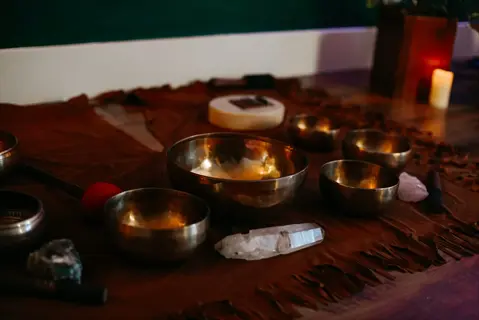 brass singing bowls and mallets arranged on suede cloth in a dimly lit space with crystals and candlelight, representing chime sound therapy tools