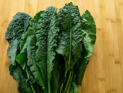 bunch of fresh kale with dark green, textured leaves on a wooden surface