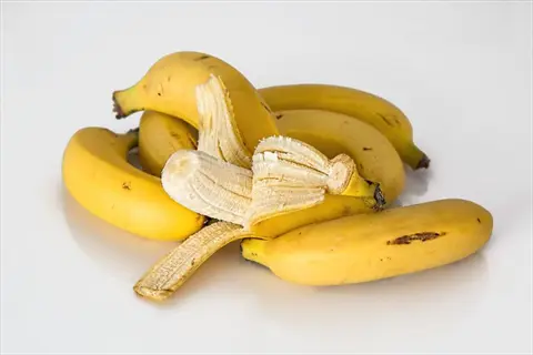 bunch of ripe fresh bananas with one partially peeled, on white background