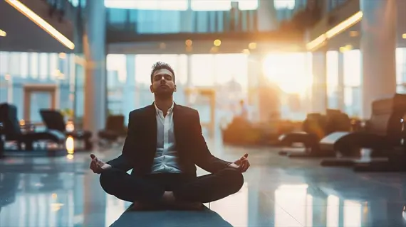 businessman in suit meditating cross-legged on office floor during workday reset, modern corporate lobby with lounge chairs and warm sunlight through glass walls