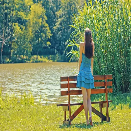 calm woman in blue dress enjoying nature by a tranquil lake with wooden bench and lush greenery