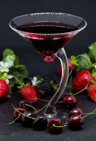 cherry juice glass with curved stem filled with dark red drink, surrounded by fresh cherries, strawberries, and blackberries - tart cherry juice