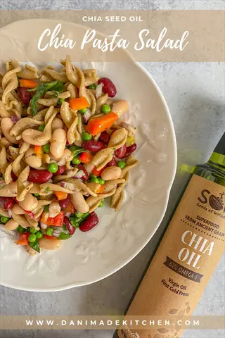 chia pasta salad with fusilli, beans, peas, and bell peppers on white plate beside chia oil bottle. overlaid text: 'chia seed oil' and 'chia pasta salad'. pasta sauce chia thickens this vibrant, healthy dish