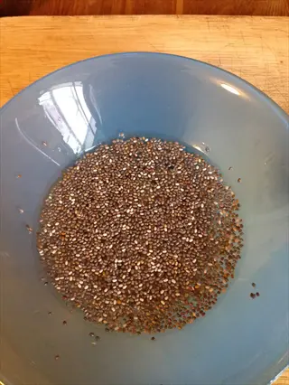 chia seeds portion in a blue bowl - close-up of tablespoon-sized amount of seeds on wooden surface