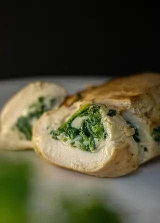 chicken breast stuffed with spinach and feta, sliced to show filling, on white plate with fresh herbs