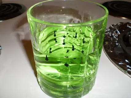chlorophyll liquid green: bright green liquid with dark suspended particles in a textured glass on a kitchen counter with stove elements visible