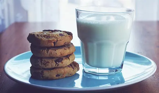 chocolate chip cookies stacked next to a glass of milk on a blue plate, representing a healthy evening snack for weight management