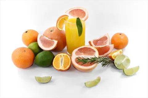 citrus fruits arrangement: oranges, grapefruits, and lemons (limes) with juice in a glass, garnished with rosemary on white background