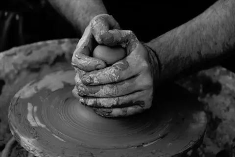 clay shaping hands: monochrome photo of hands working on spinning potter's wheel, sculpting raw clay into form - embodying sculpture through tactile creation