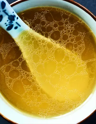 close-up of a bone broth bowl with spoon, showing golden bubbles and oil swirls in a decorative dish