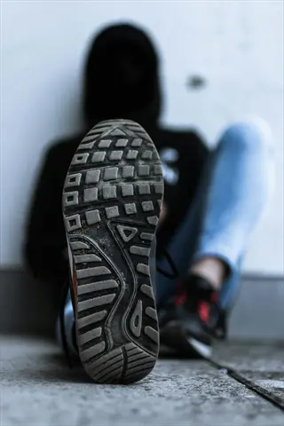 close-up of a worn sneaker sole showing tread wear patterns with blurred hooded figure in background
