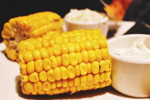 close-up of golden corn on the cob with plump kernels beside creamy dips, highlighting tactile food texture through detailed surface ridges and smooth sauce consistency