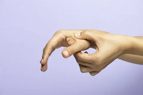 close-up of one hand applying pressure to the thumb base pressure point on another hand against a light purple background