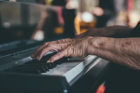 close-up of piano hands: elderly person's weathered hands playing piano keys in softly lit setting