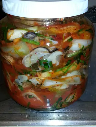 close view of a sealed jar filled with red kimchi, a fermented food, on a tiled surface