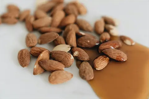 closeup of raw almonds with some coated in syrup on a light surface