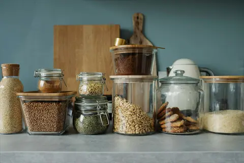 collection of glass food containers with bamboo lids storing grains, seeds, and cookies on a kitchen counter, organized pantry setup